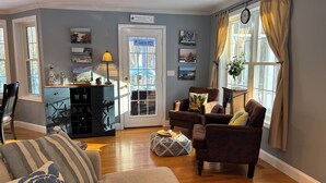 A cozy living room with a sofa, armchair, and a dining area with a cabinet and table. - Half-Acre Coastal Retreat- Hot tub and walk to town! (Ogunquit)