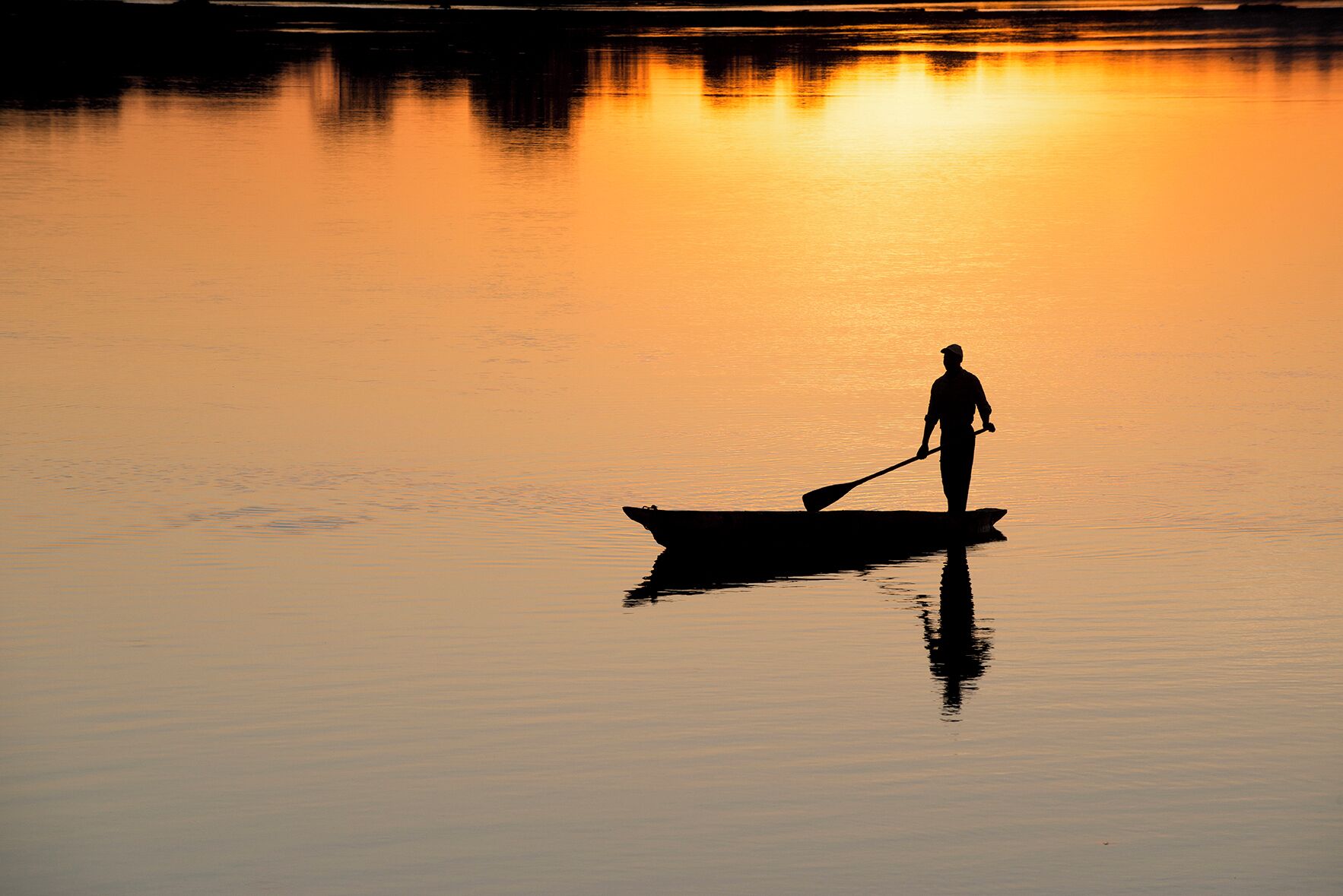Silueta de una persona remando en un bote sobre aguas tranquilas durante la puesta de sol.
