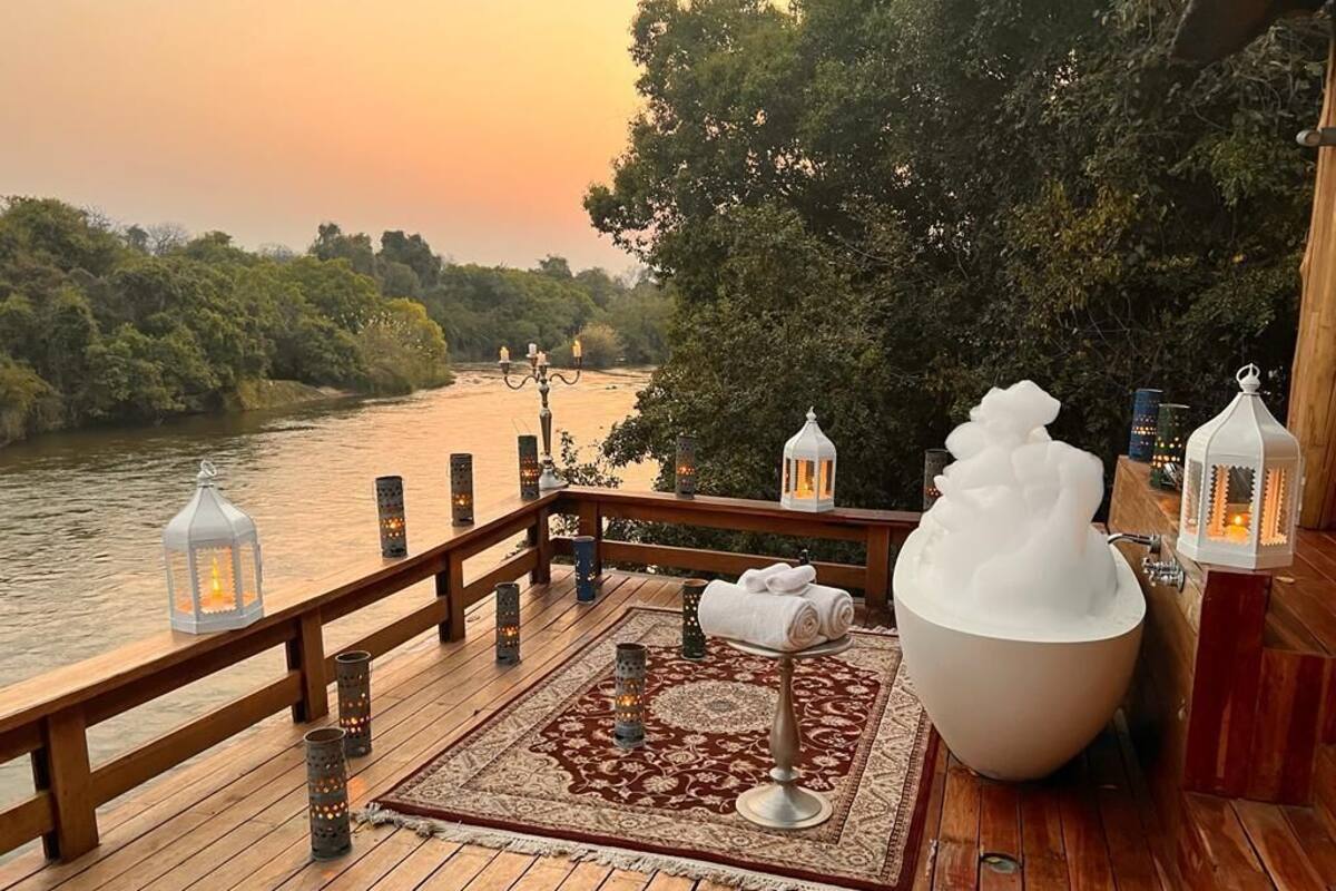 A wooden deck with a view of a river, surrounded by trees. There are lanterns and a large white urn on the deck.