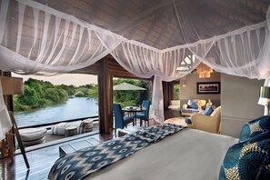 Un dormitorio con una cama grande, un espacio de estar con una mesa y sillas, y vistas al río.