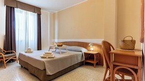 Una habitación de hotel con cama, una silla, una mesita pequeña y una mesita de noche.
