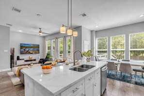 A modern kitchen with a large island, a dining area with a view, and a living room with a flat-screen TV. - 5 BR Houston Retreat - Private Loft + Huge Deck - Sleeps 12 (Houston)