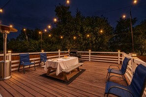 An outdoor deck with a table and chairs, string lights, and a grill. - 5 BR Houston Retreat - Private Loft + Huge Deck - Sleeps 12 (Houston)