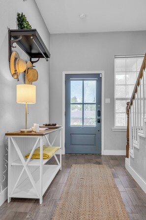 A modern entryway with a blue door, a white console table with a lamp, a wooden bench, and a decorative wall piece. - 5 BR Houston Retreat - Private Loft + Huge Deck - Sleeps 12 (Houston)