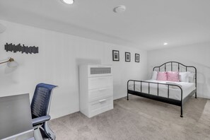 A bedroom with a bed, a desk, a chair, a dresser, and a wall-mounted shelf.