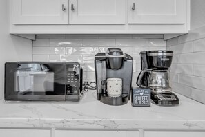 A kitchen with a microwave, coffee maker, and coffee pot on the counter.