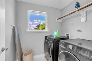 A laundry room with two washing machines, a window with a view of trees, and a shelf with a blue item.