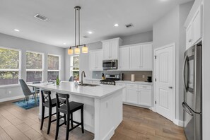 A modern kitchen with white cabinetry, a central island with bar stools, stainless steel appliances, and a pendant light fixture. - 5 Bed Home - Garage Apartment -Large Backyard Deck - BBQ Grill (Houston)