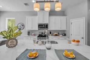 A modern kitchen with white cabinets, a stainless steel sink, and a central island with a vase and oranges. - 5 BR Houston Retreat - Private Loft + Huge Deck - Sleeps 12 (Houston)