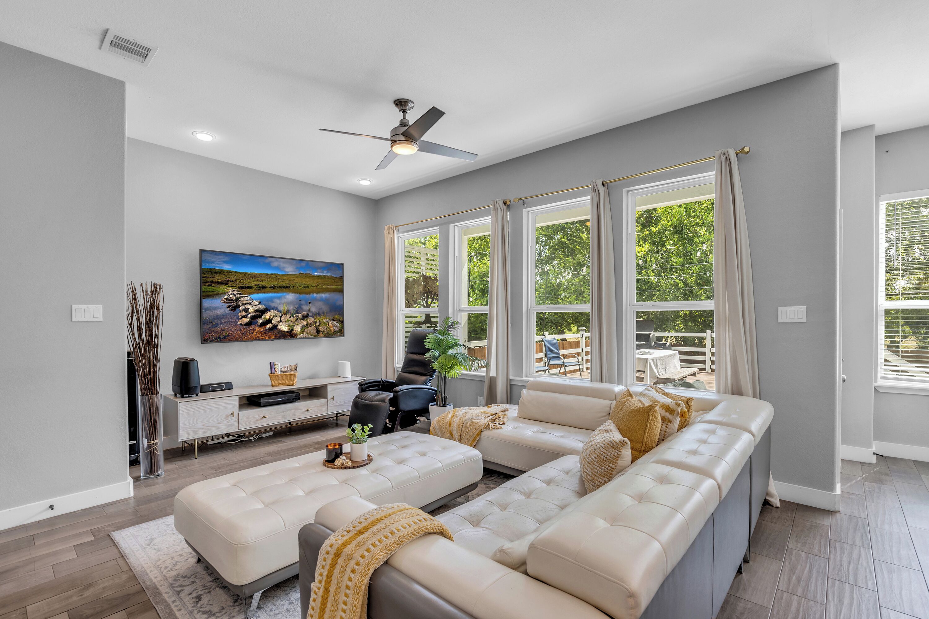 A modern living room with a sectional sofa, a flat-screen TV mounted on the wall, and a ceiling fan.