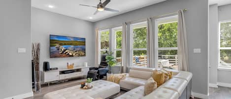 A modern living room with a sectional sofa, a flat-screen TV mounted on the wall, and a ceiling fan.