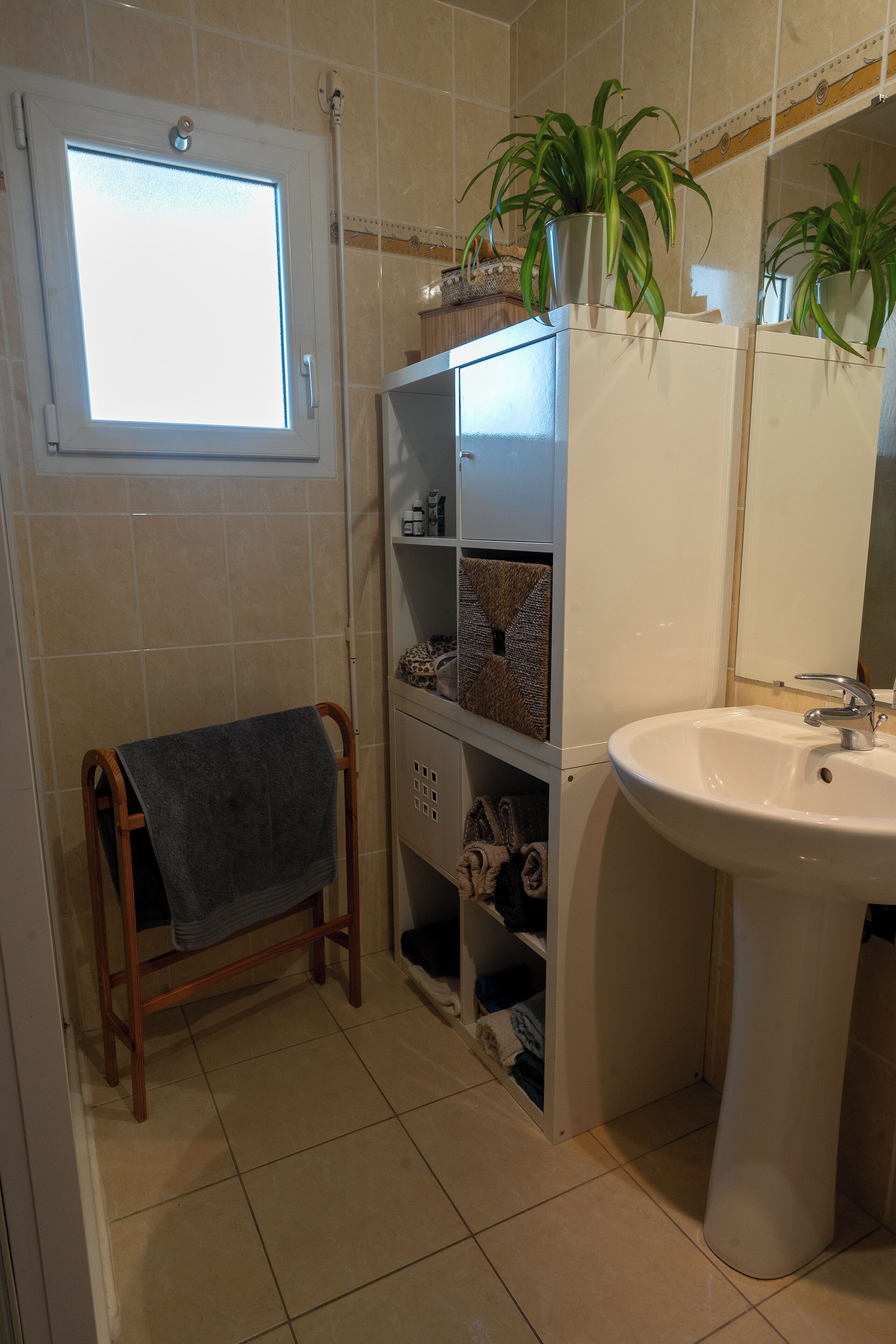 A bathroom with a window, a sink, shelves with toiletries, and a towel rack.
