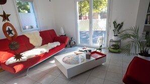 Una sala de estar moderna con un sofá rojo, una mesa de centro blanca y un amplio ventanal corredero que da a un patio.