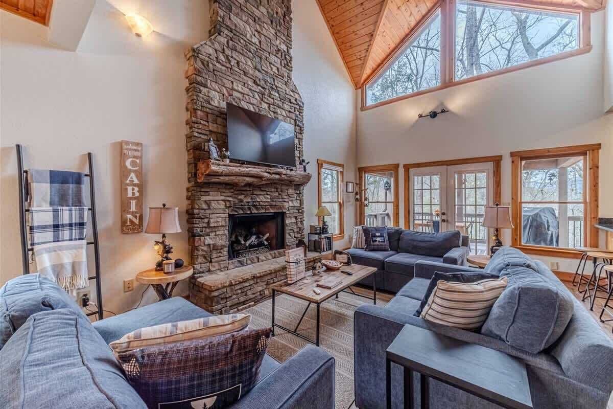 A cozy living room with a stone fireplace, a television, and a large window.