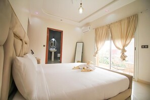 A hotel room with a large bed, a bathroom mirror, and a view of the outside balcony.