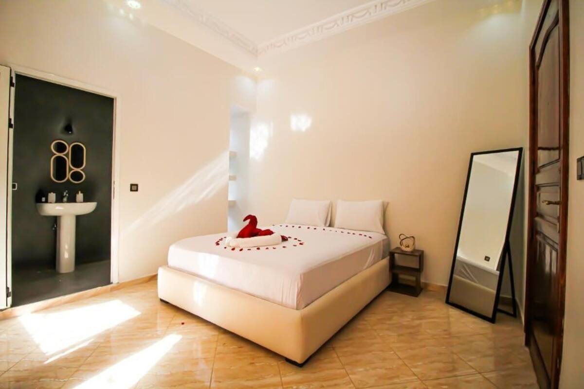 A bedroom with a bed, a bedside table, a mirror, and a door leading to a bathroom.