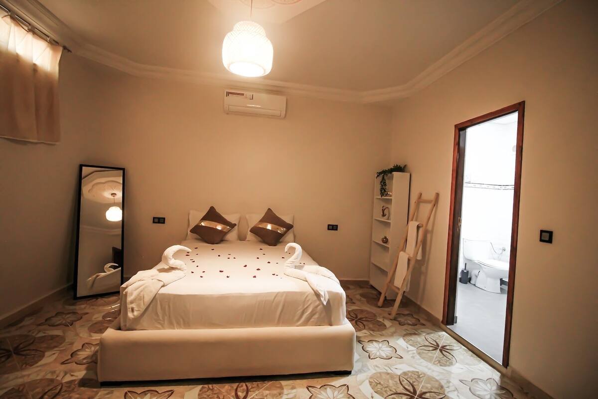 A hotel room with a large bed, a mirror, an air conditioning unit, a wardrobe, and a bathroom visible through an open door.