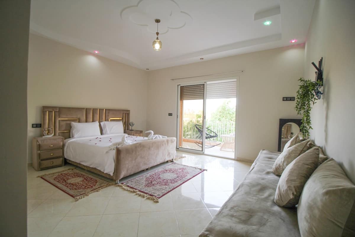 A bedroom with a bed, a sofa, a nightstand, a dresser, and a sliding glass door leading to a balcony.