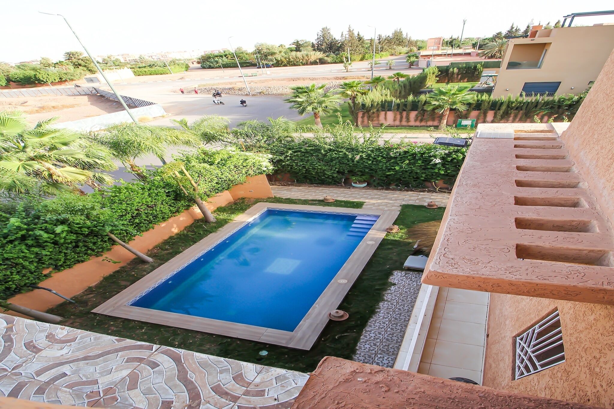 Piscina rodeada de vegetación, una escalera y vista a una carretera con vehículos.