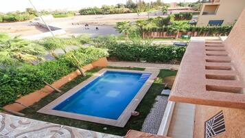 Piscina rodeada de vegetación, una escalera y vista a una carretera con vehículos.