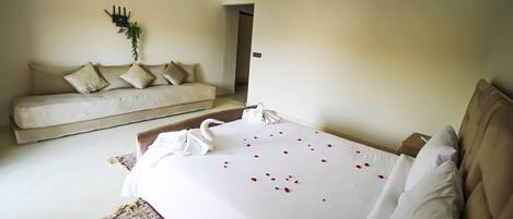 A hotel room with a bed, a sofa, a wall-mounted air conditioner, and a door leading to another room.