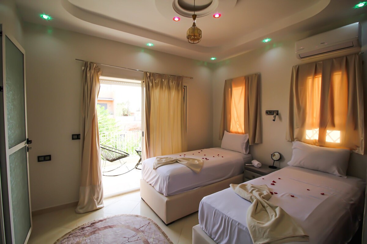 Camera d'albergo con due letti, una ventola a soffitto, un climatizzatore e un balcone con una sedia.