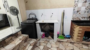 Uma cozinha compacta com piso de ladrilho de pedra, uma lixeira preta, uma pia pequena e uma vassoura encostada na parede.