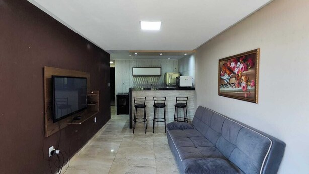 Uma sala de estar com TV, sofá e área de cozinha com balcão.