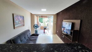 Uma sala de estar com um sofá, um ventilador e uma TV sobre uma prateleira de madeira.