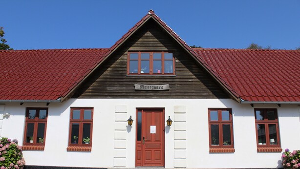 A traditional building with a red-tiled roof, a central wooden door, and a sign above the door. - Stay Billund – lovely holiday apartment just 5 minutes from Legoland (Vandel)