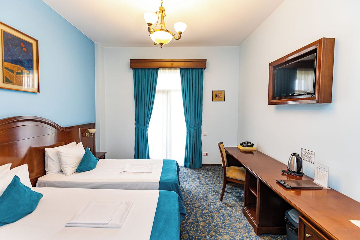 Ett hotellrum med två sängar, ett skrivbord, en tv och ett fönster med gardiner.