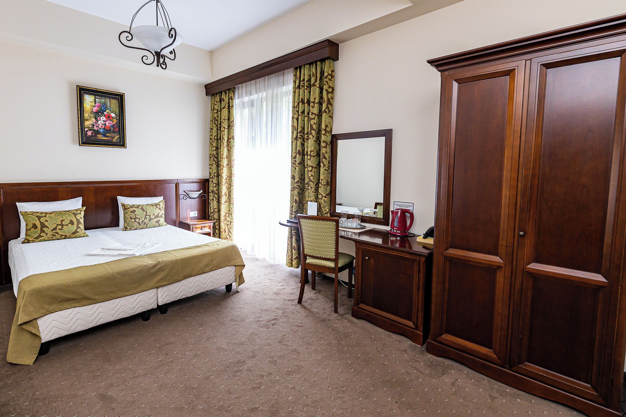 Una habitación de hotel con cama, escritorio, silla, armario, espejo y un cuadro en la pared.