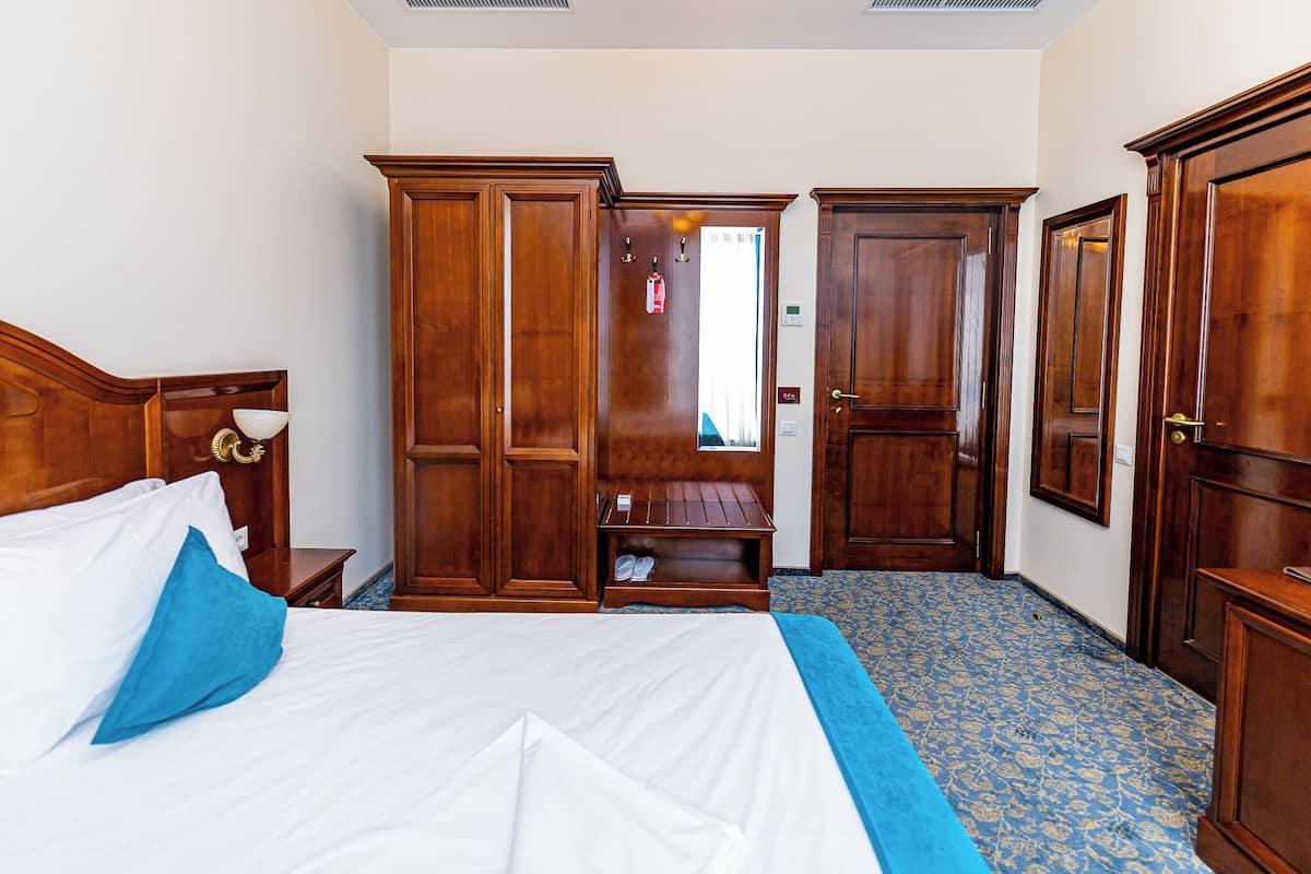 Ett hotellrum med en stor säng, en garderob i trä och en bänk.