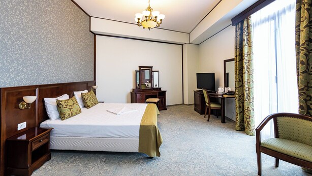 A hotel room with a large bed, a desk, a chair, a television, and a chandelier. - HOTEL DIESEL (Bucharest)
