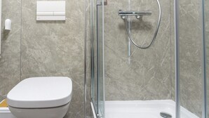 Un baño moderno con inodoro, ducha con mampara de vidrio y pared revestida de mármol.