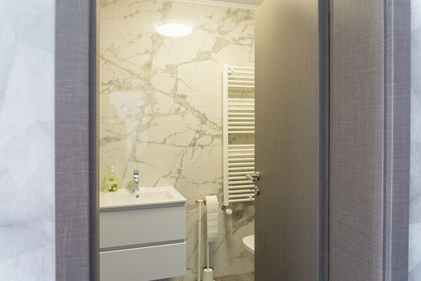 Un baño con pared de mármol, un lavamanos blanco, un perchero y un inodoro.
