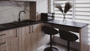 Una cocina moderna con armarios de madera, encimera negra, un lavamanos y dos taburetes negros.