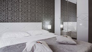 Un dormitorio moderno con papel tapiz estampado, cabecera capitonada, un espejo grande y una mesita de noche con lámpara.