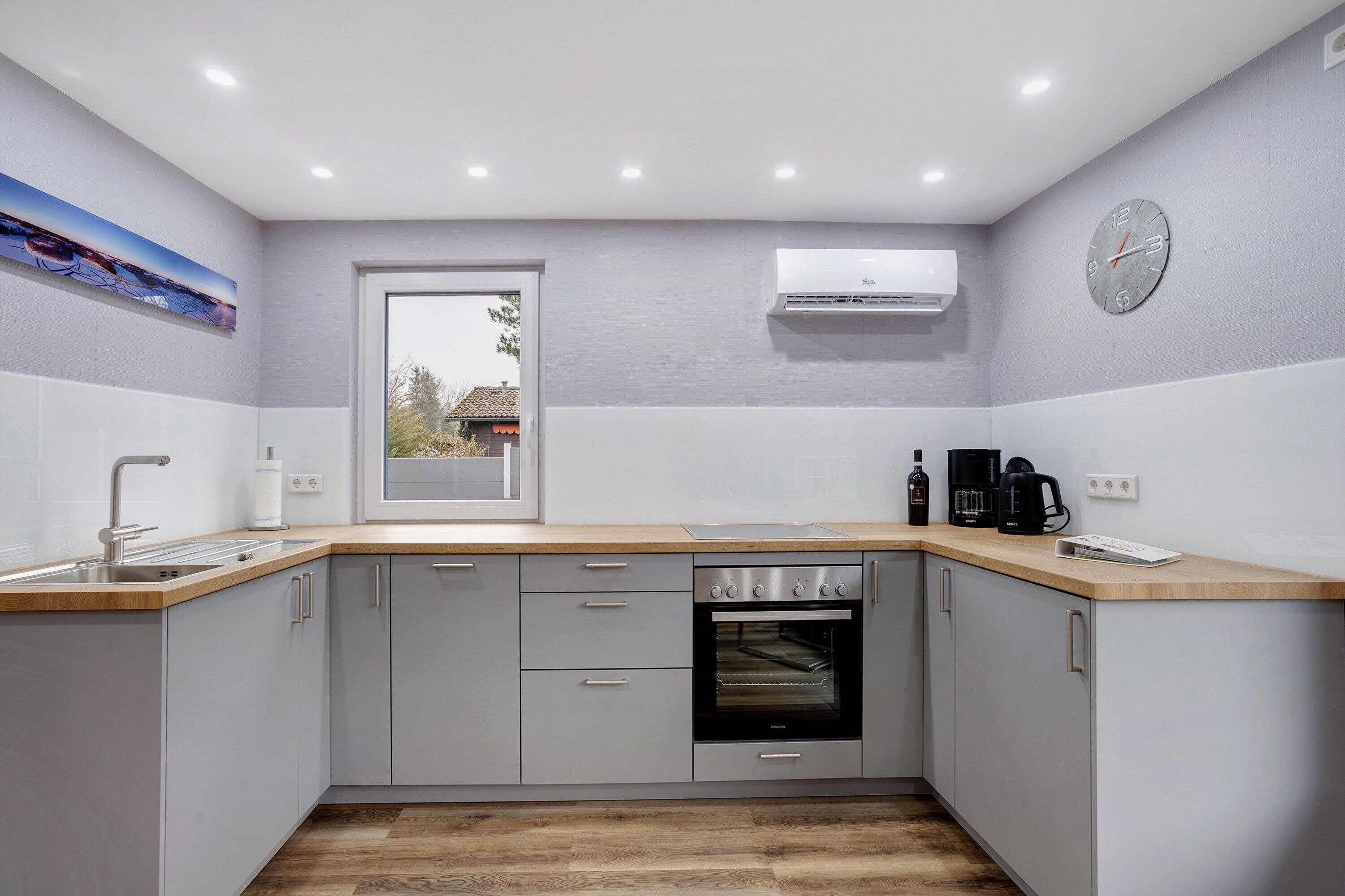 A modern kitchen with grey cabinets, a wooden countertop, an oven, and a window with a view.