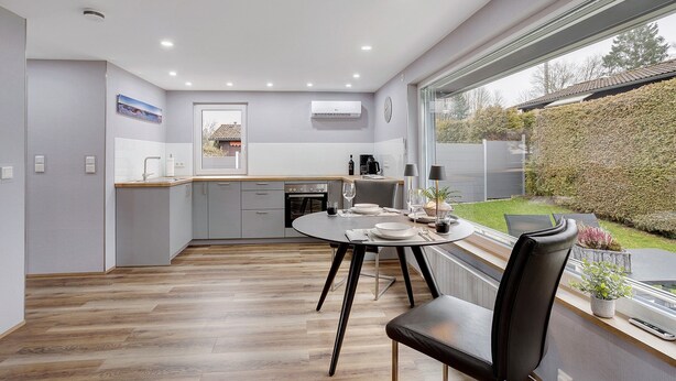 A modern kitchen with a dining area, a large window, and a view of the garden. - Holiday Home Adelon with Private Terrace, Wi-Fi, and Air Conditioning at Lake Möhnesee (Möhnesee)