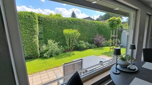 A room with a large window overlooking a well-maintained garden, a small table with a lamp, and a chair. - Holiday Home Adelon with Private Terrace, Wi-Fi, and Air Conditioning at Lake Möhnesee (Möhnesee)