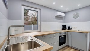 A modern kitchen with a stainless steel sink, a window, a wall-mounted clock, and a built-in oven. - Holiday Home Adelon with Private Terrace, Wi-Fi, and Air Conditioning at Lake Möhnesee (Möhnesee)