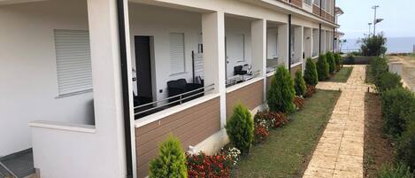 A modern hotel with a covered outdoor seating area, a well-maintained garden, and a clear view of the sea.