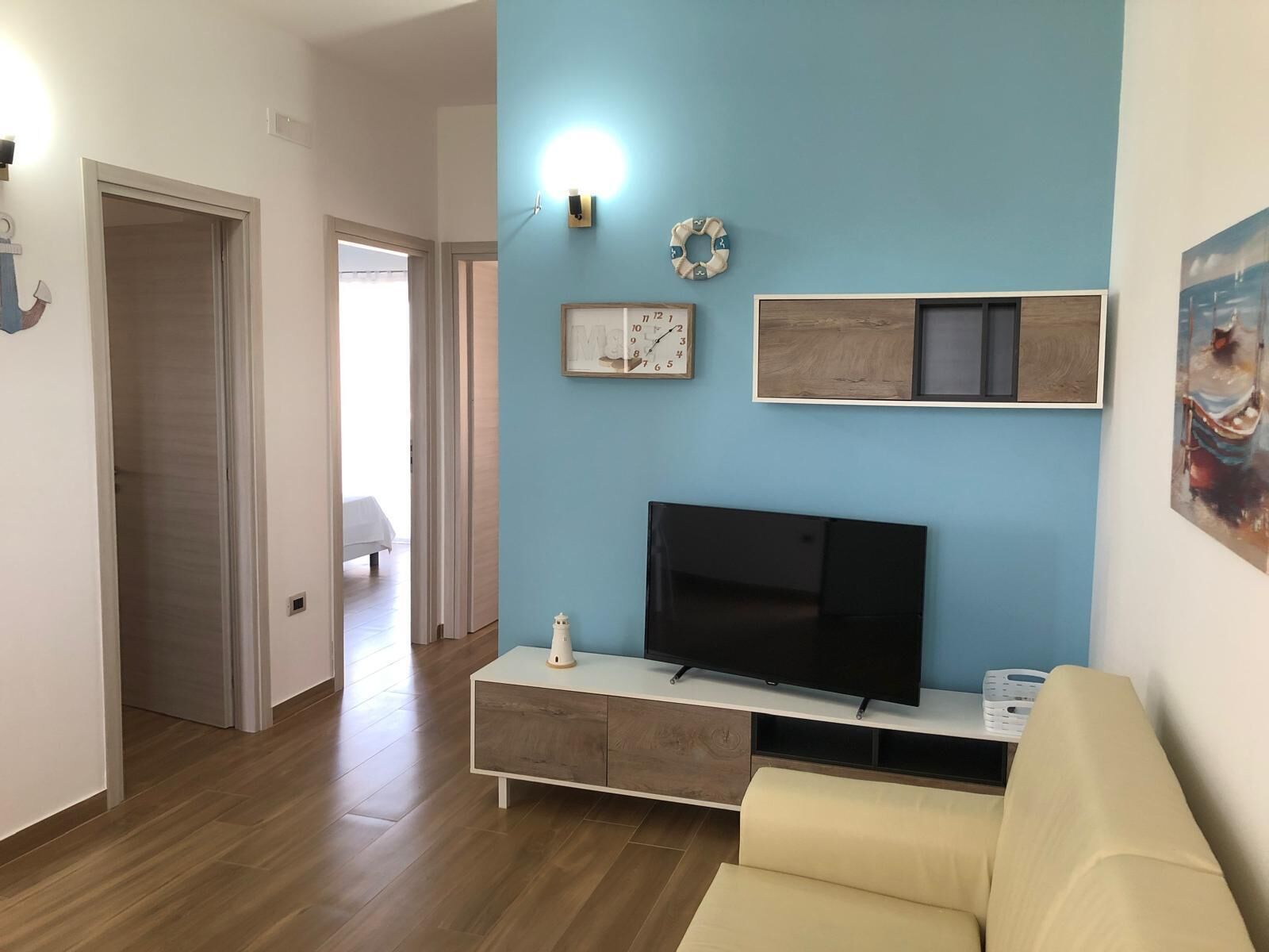 Een woonkamer met een televisie op een witte console, een beige bank en een blauwe muur met een klok en een ingelijste foto.