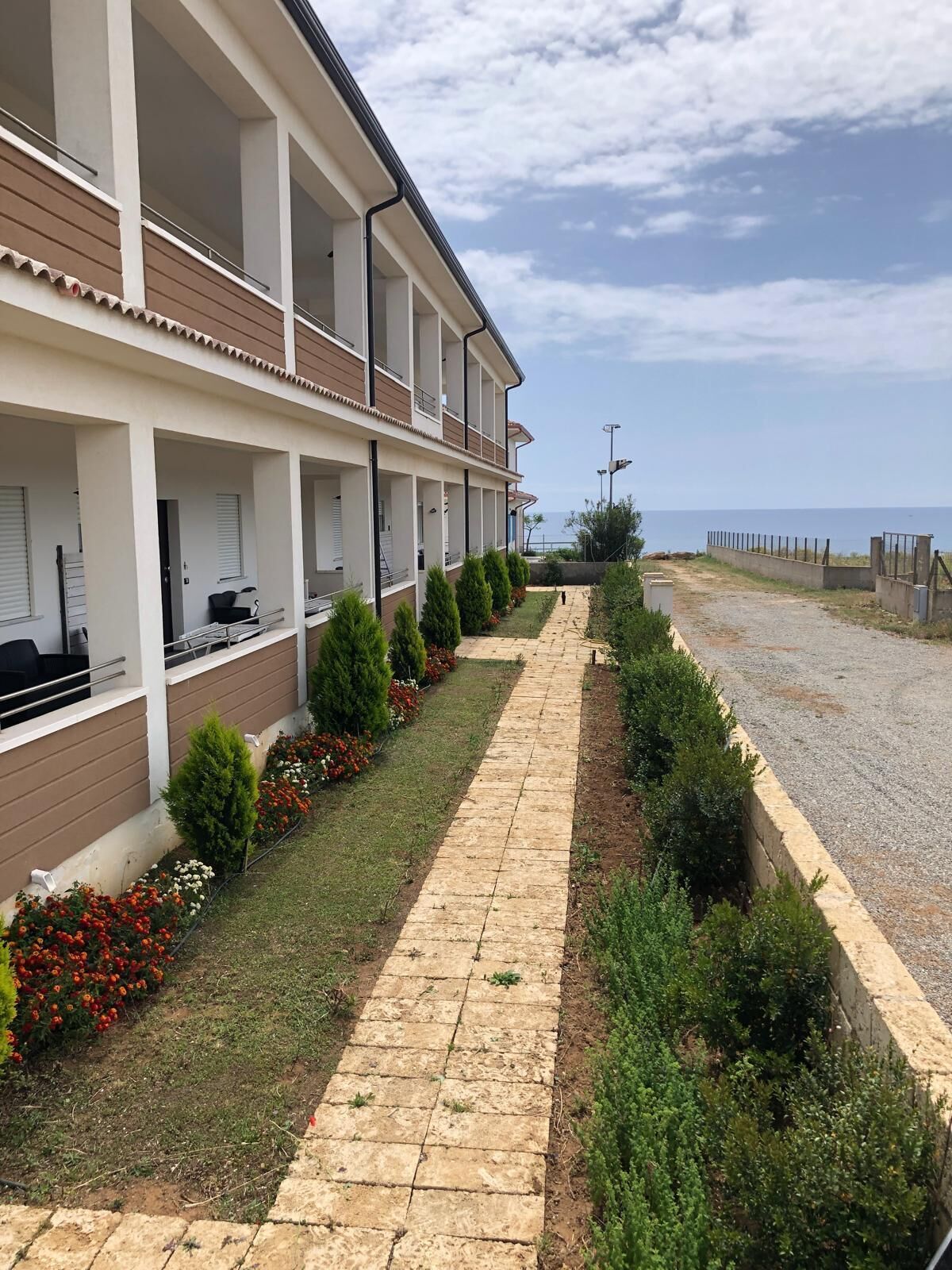 Un edificio moderno con un área exterior cubierta, un sendero pavimentado y vista al mar.