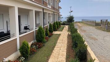 Un edificio moderno con un área exterior cubierta, un sendero pavimentado y vista al mar.