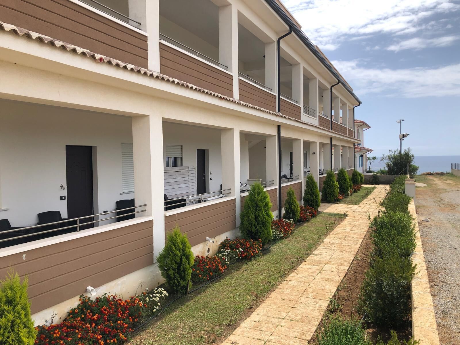 Un hotel de varios pisos con balcones, un camino pavimentado y vista al mar.
