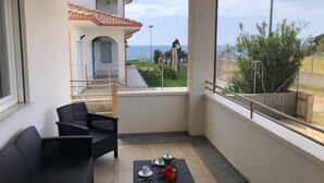 Un balcon agrémenté de meubles en osier, une petite table avec des tasses et des fleurs, et une vue sur un bâtiment doté d’un toit en tuiles et d’un portail.