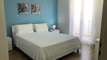 Un dormitorio con una cama grande, dos almohadas blancas, una mesita de noche con una lámpara y dos obras de arte en la pared.