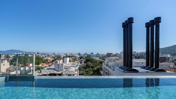A rooftop infinity pool with a city view, large black chimneys, and a clear blue sky. - Ap in a Condominium With gym in Jurere Vox0210 (Florianópolis)